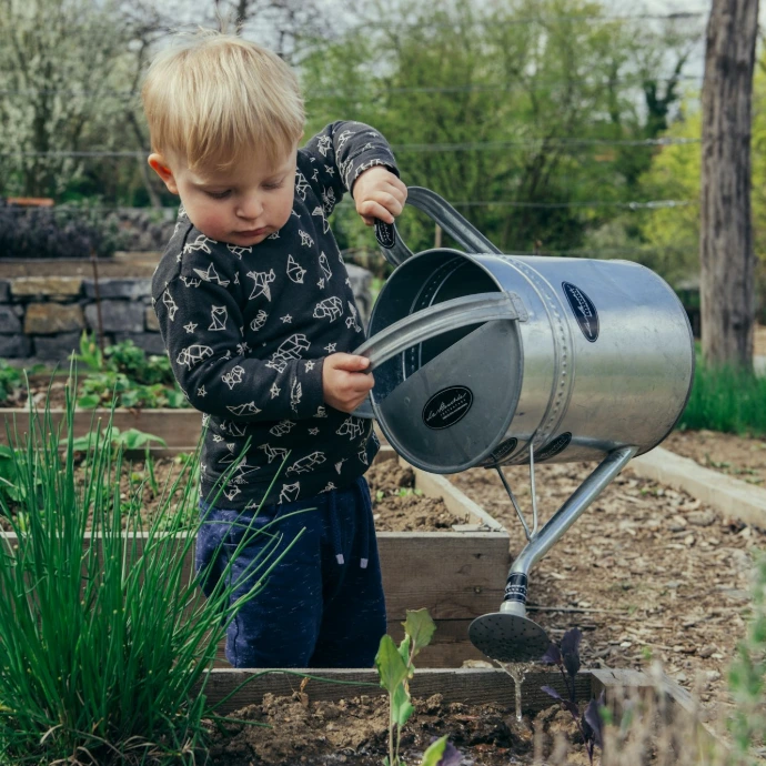 boy in black and white long sleeve shirt standing beside gray metal watering can during daytime